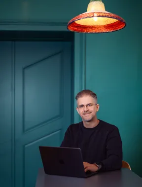 Martin Gratzer sitting at a desk with a laptop, in front of a teal wall
